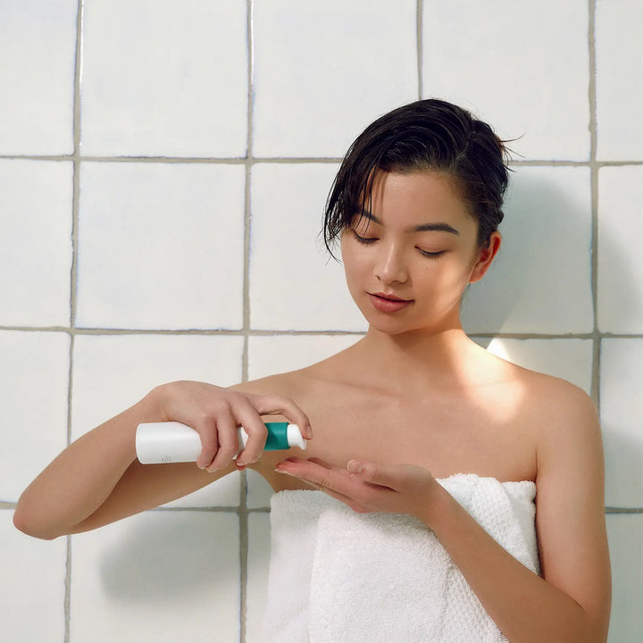 fille peau blanche coréenne qui tient le nettoyant purifiant visage dans une salle de bain à carreaux avec serviette autour du corps