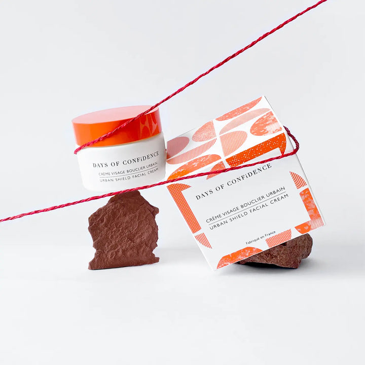 photo packshot sur fond blanc packaging eco responsable crème hydratante visage bouclier urbain boite blanche et rouge sur cristaux pierre marron avec ficelle rouge qui les tient 