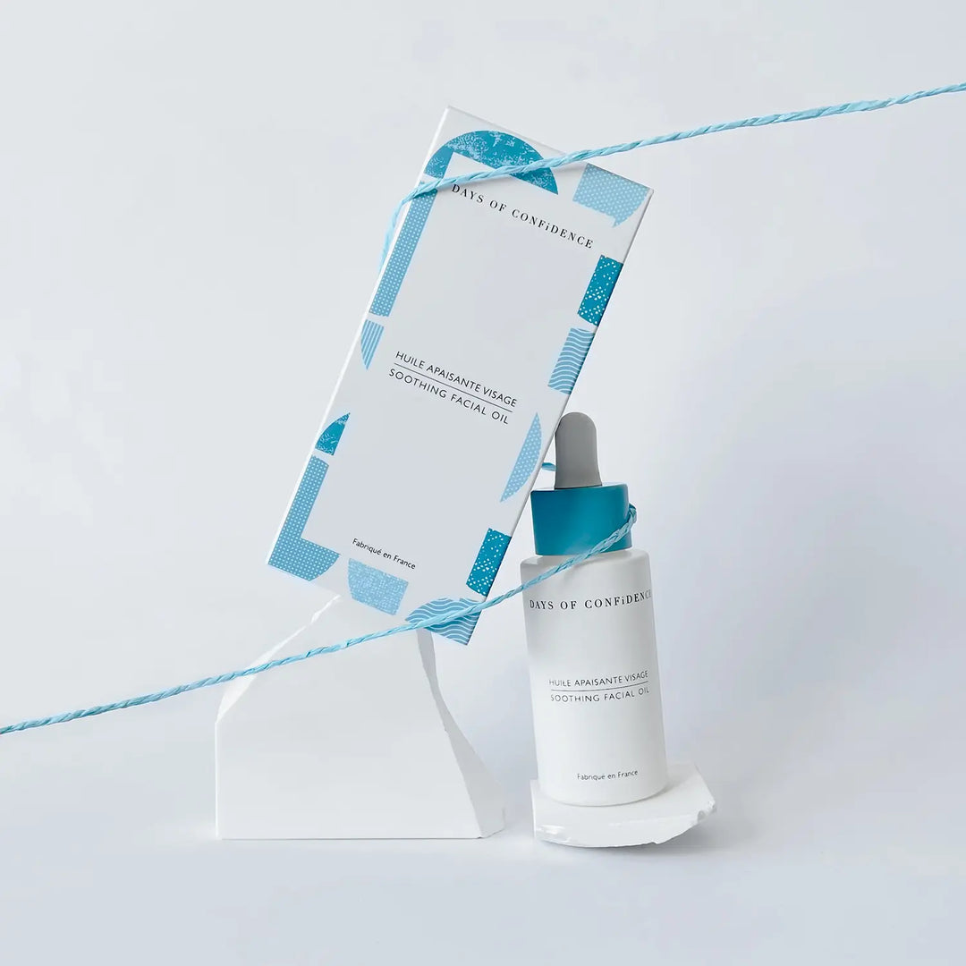 photo packshot sur fond blanc packaging éco responsable de l’huile visage apaisante boite blanche et bleue sur pierre blanche avec ficelle bleue qui les tient