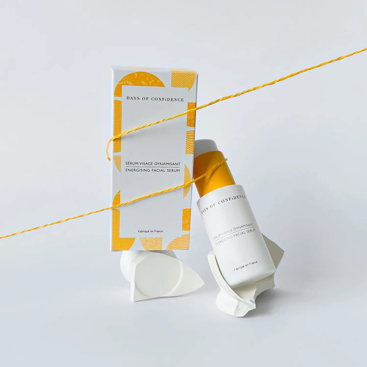 photo packshot sur fond blanc packaging blanc et jaune sérum dynamisant visage ingrédients bio acide hyaluronique prépare la peau et diminue les rougeurs sur pierre blanche avec ficelle jaune qui les tient