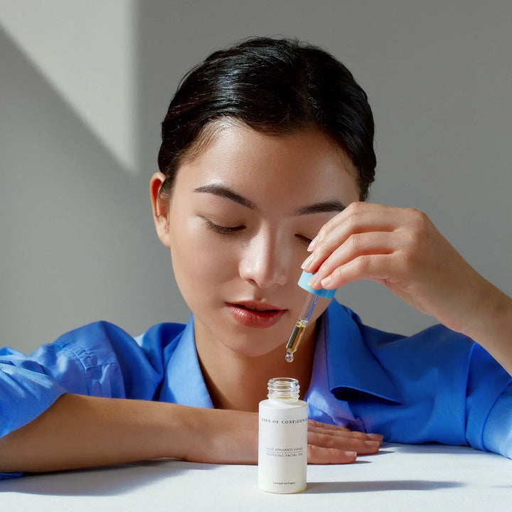 fille eurasienne vêtue d’une chemise bleue qui tient dans ses mains pipette bleu produit huile visage apaisante days of confidence